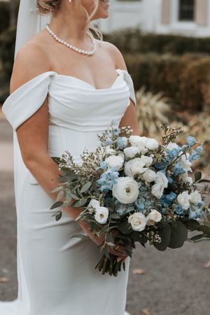 White bridal bouquet features delicate blue accents and eucalyptus greenery against an elegant white wedding dress.