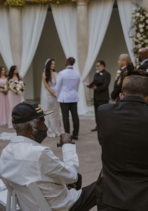 Guests seated at an outdoor wedding ceremony with white curtains and floral decorations.