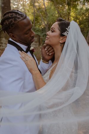 Wedding couple shares intimate moment with flowing veil in golden outdoor setting.