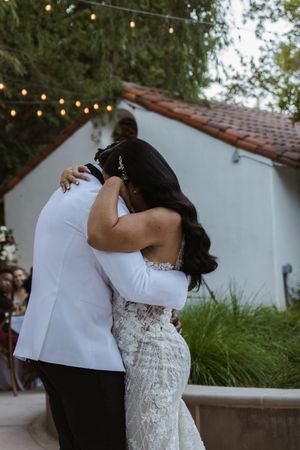 Couple shares an intimate dance moment under twinkling lights at an outdoor wedding venue.
