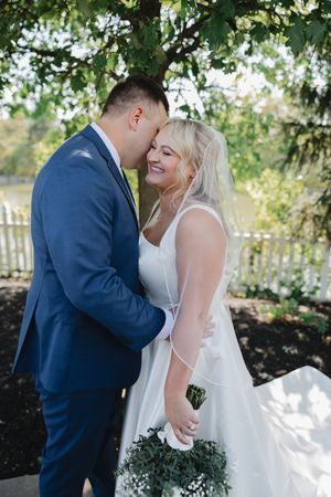 A romantic wedding moment captured in a garden setting with a couple in blue suit and white dress sharing an intimate embrace.