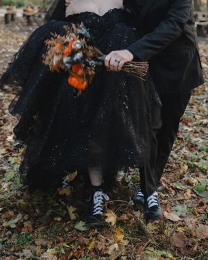 Feet in black shoes and dress shoes stand together on fallen autumn leaves in an outdoor setting.