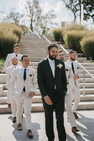 Wedding party poses on outdoor stairs with groomsmen in light suits and groom in dark suit.
