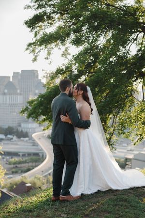 A couple shares an intimate moment on a hilltop overlooking a cityscape during their wedding photoshoot.