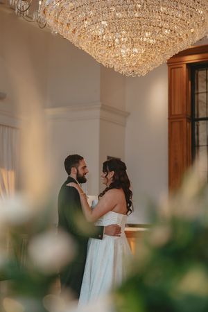 Couple shares intimate moment under ornate crystal chandelier during wedding reception.