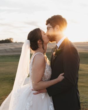 A romantic sunset wedding portrait shows a couple sharing a kiss on a golf course with golden light behind them.