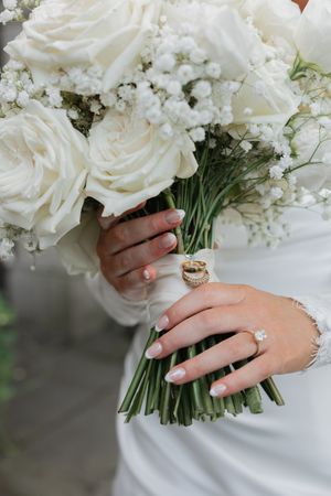 A close-up sequence of white roses and baby's breath wedding bouquet held by hands with elegant rings.