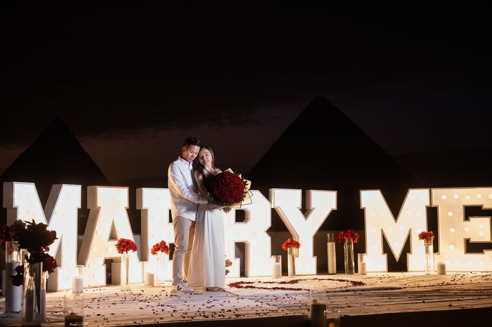 Glowing white MARRY ME letters create a romantic proposal backdrop at twilight.