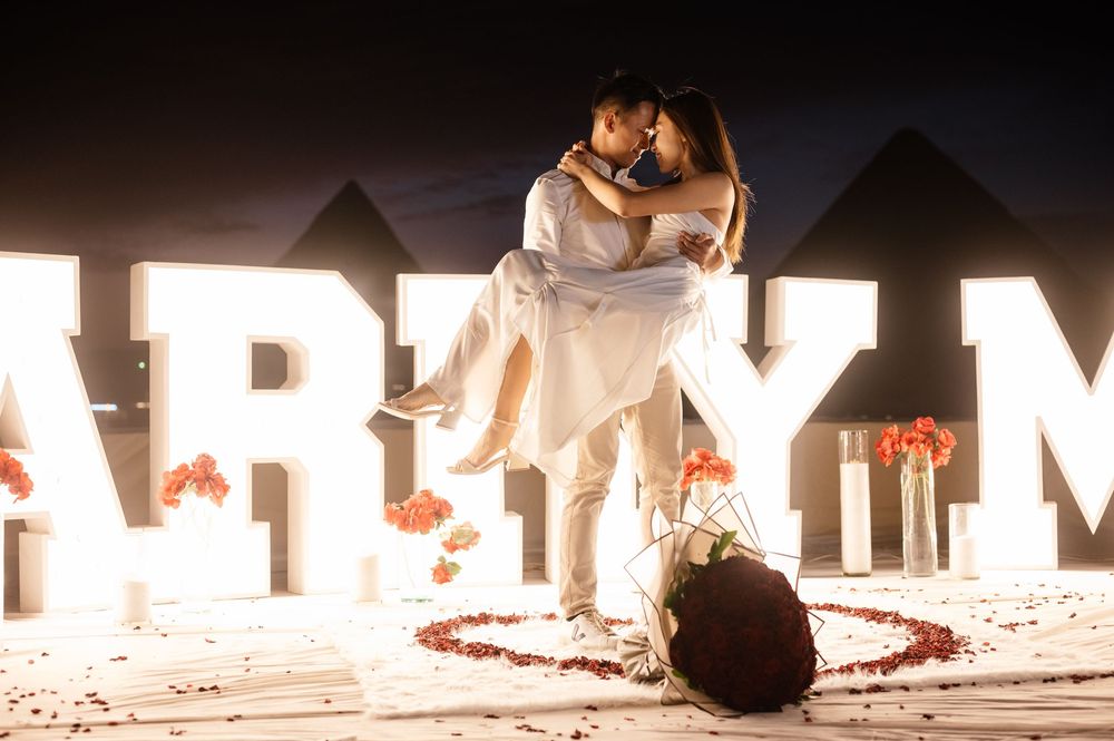 Illuminated white MARRY ME sign creates a dramatic nighttime wedding proposal scene.