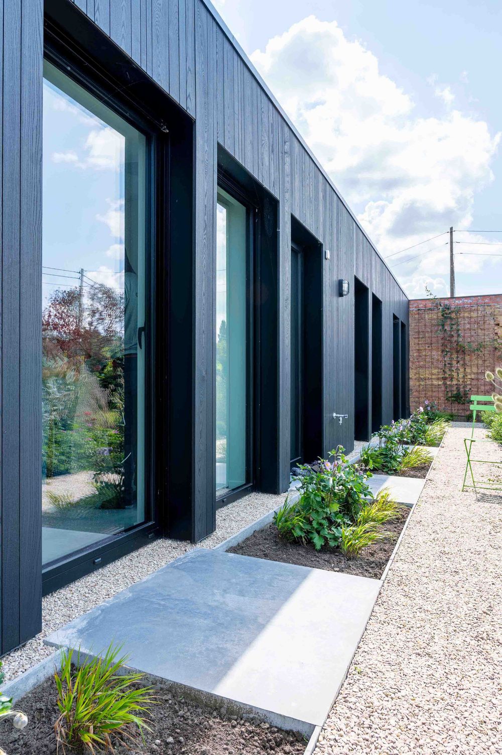 Modern building exterior with black panels and large glass windows along gravel pathway.