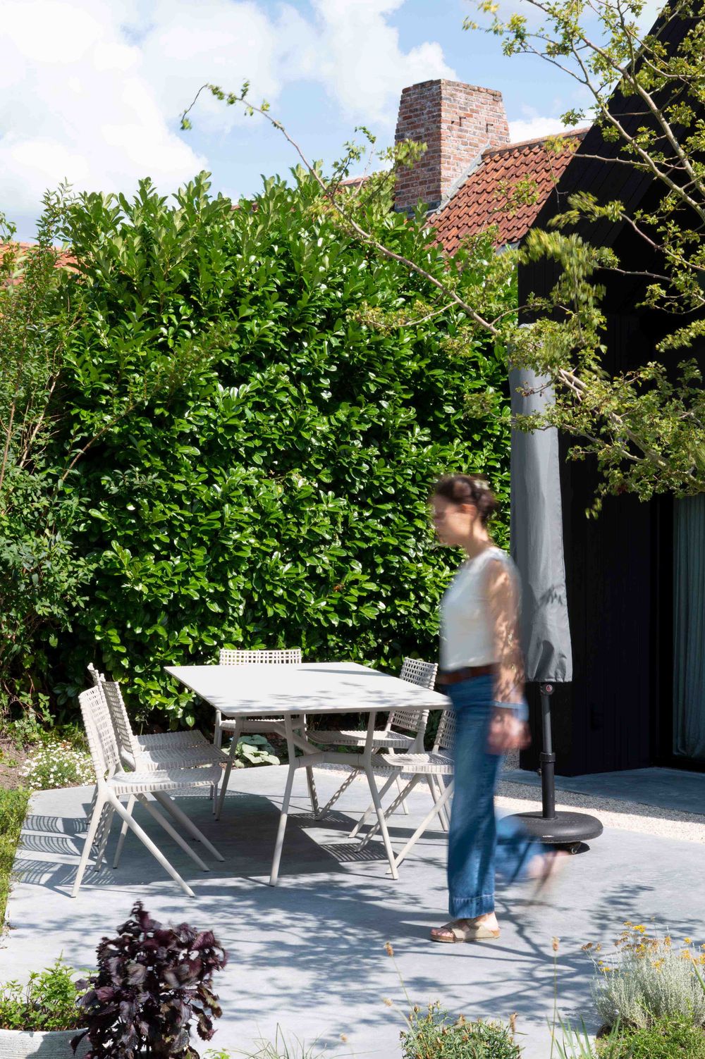 Outdoor seating area with white furniture surrounded by lush garden landscaping.