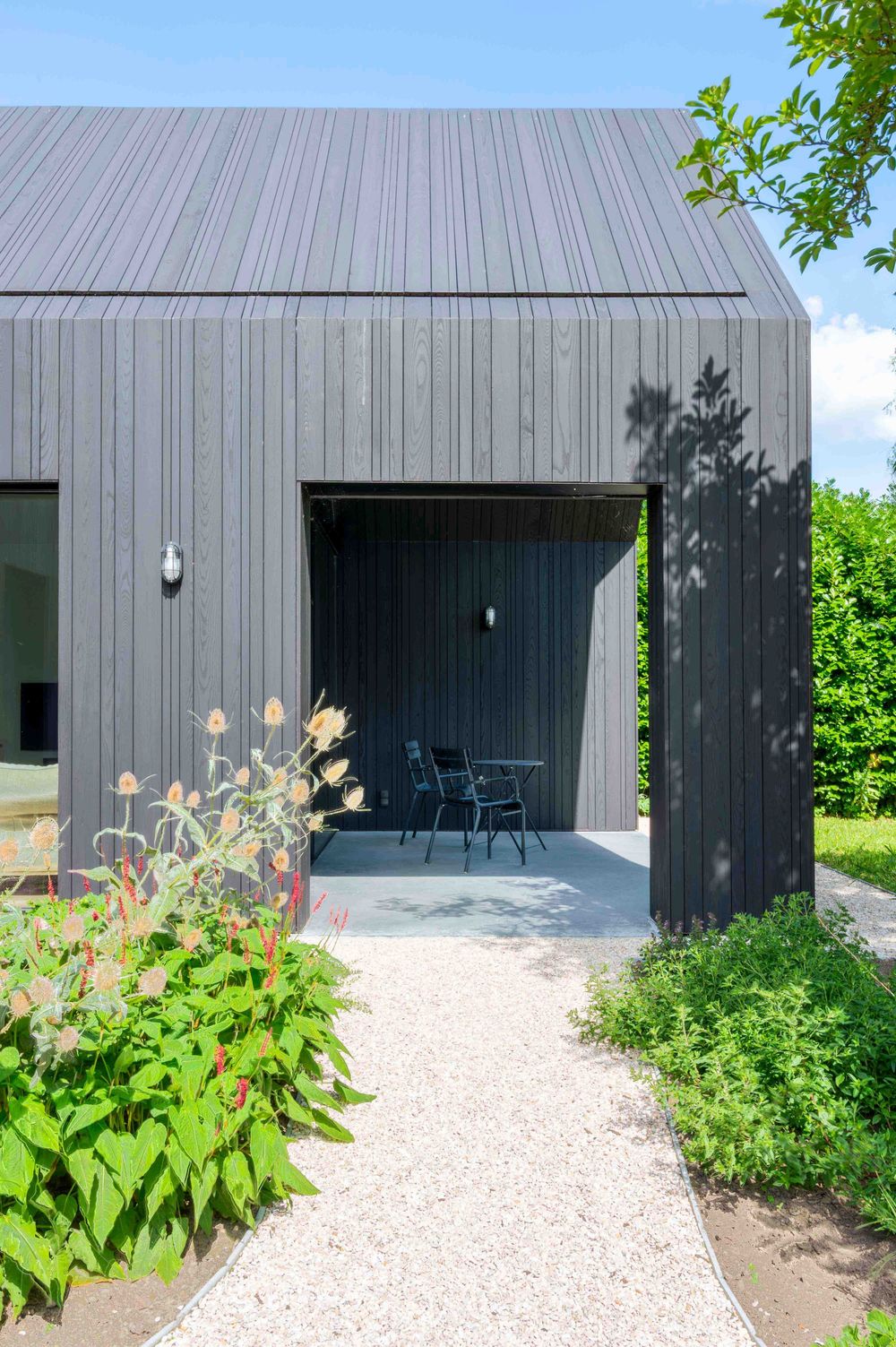 Contemporary black building facade with gravel pathway and colorful garden flowers blooming along the sides.