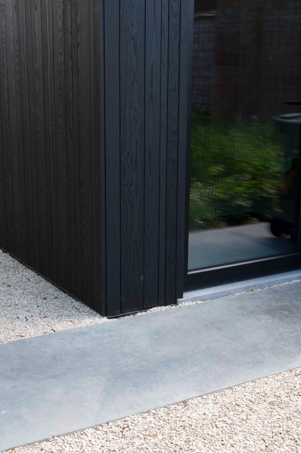 Close-up detail of dark wood siding and concrete foundation with white gravel border.