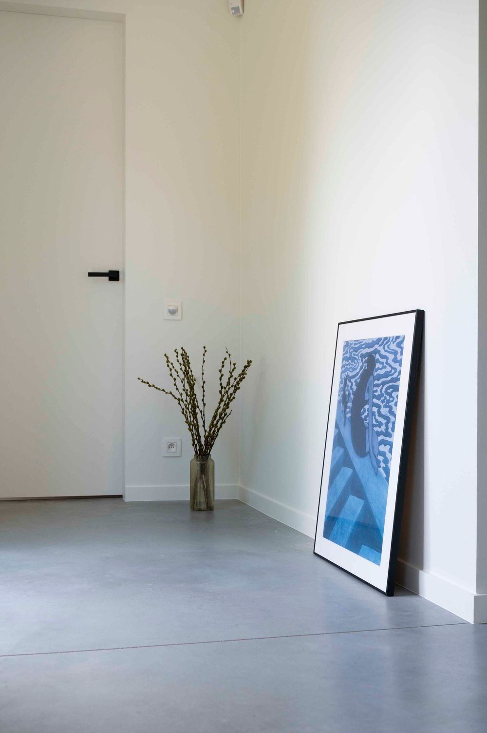 Minimalist interior space with concrete floors, white walls and framed artwork leaning against the wall.