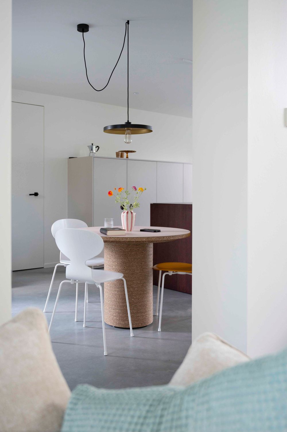 Eetkamer met witte stoelen onder een minimalistische hanglamp op een grijze polybeton vloer.