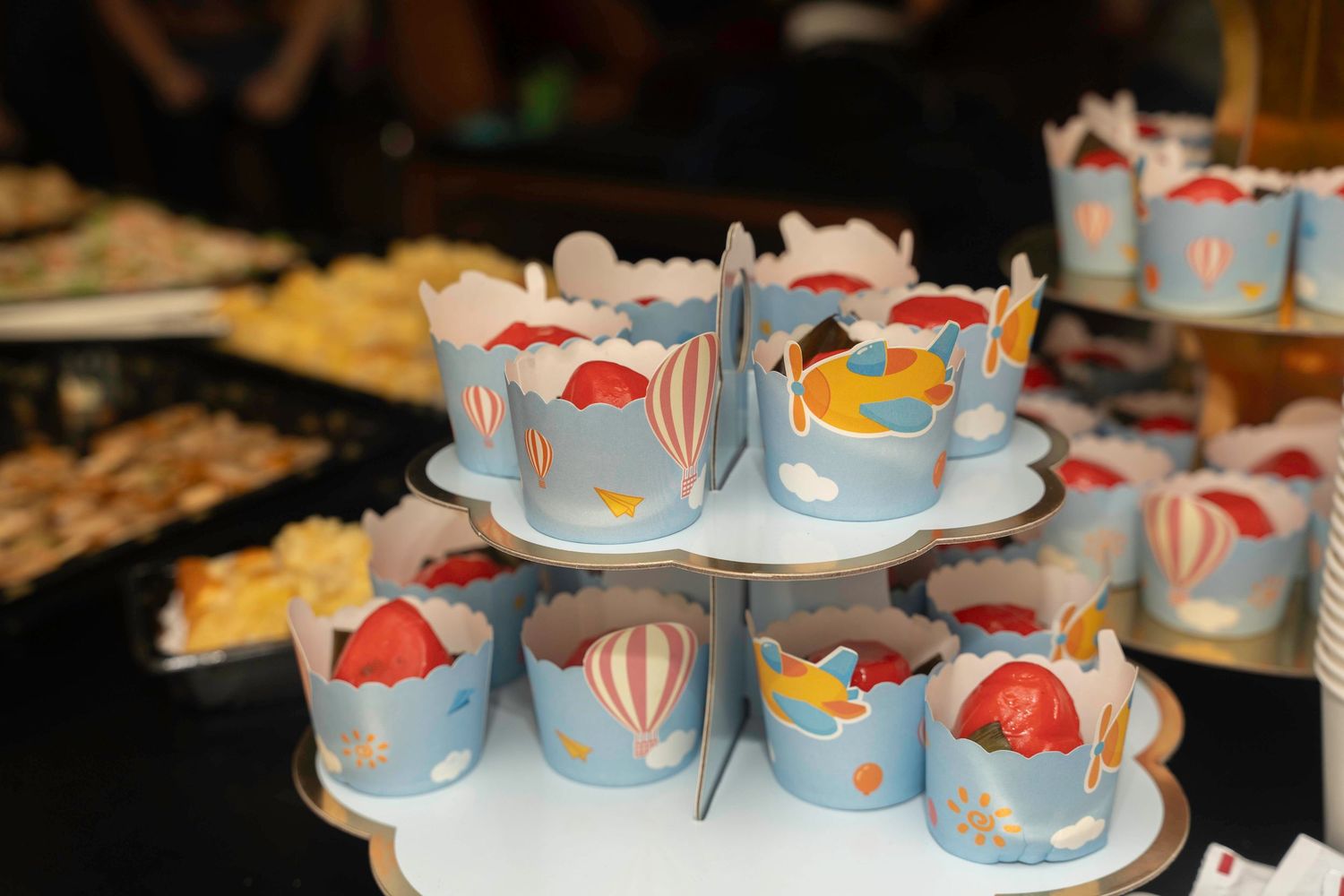 Tiered tray display of blue and white decorated cupcakes with red accents on a dessert table.