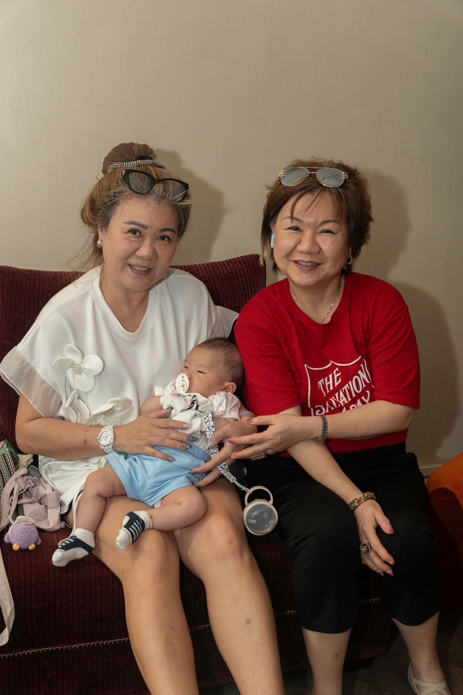 Two people sitting on a brown couch share joyful moments with a small baby in a light blue outfit.