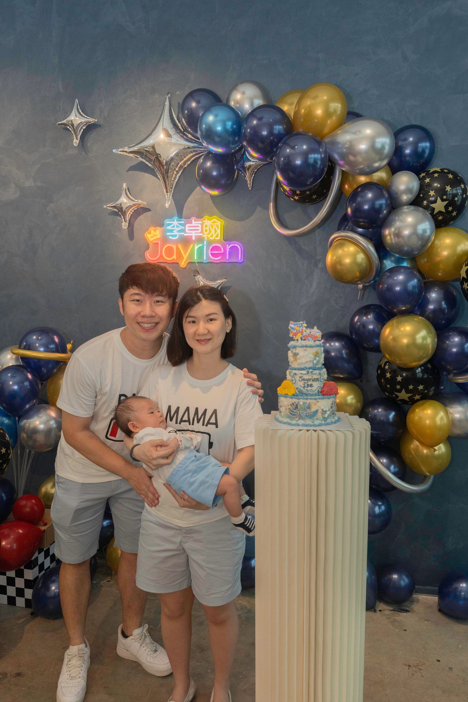 Festive birthday party set up with blue and gold balloon arch, white decorative column and three-tier cake.