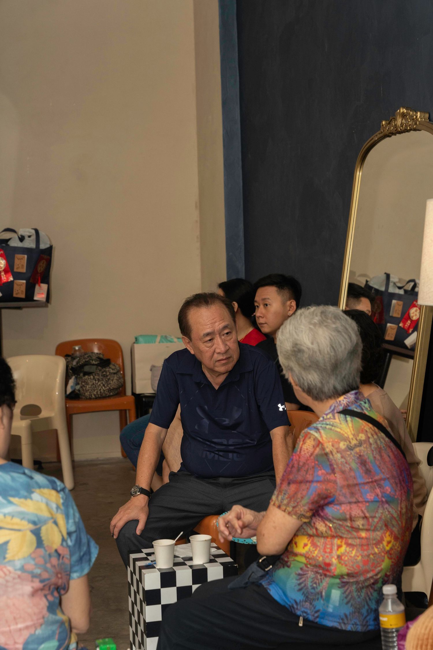 People gathered in a room playing a board game on a checkered surface with a decorative mirror in the background.