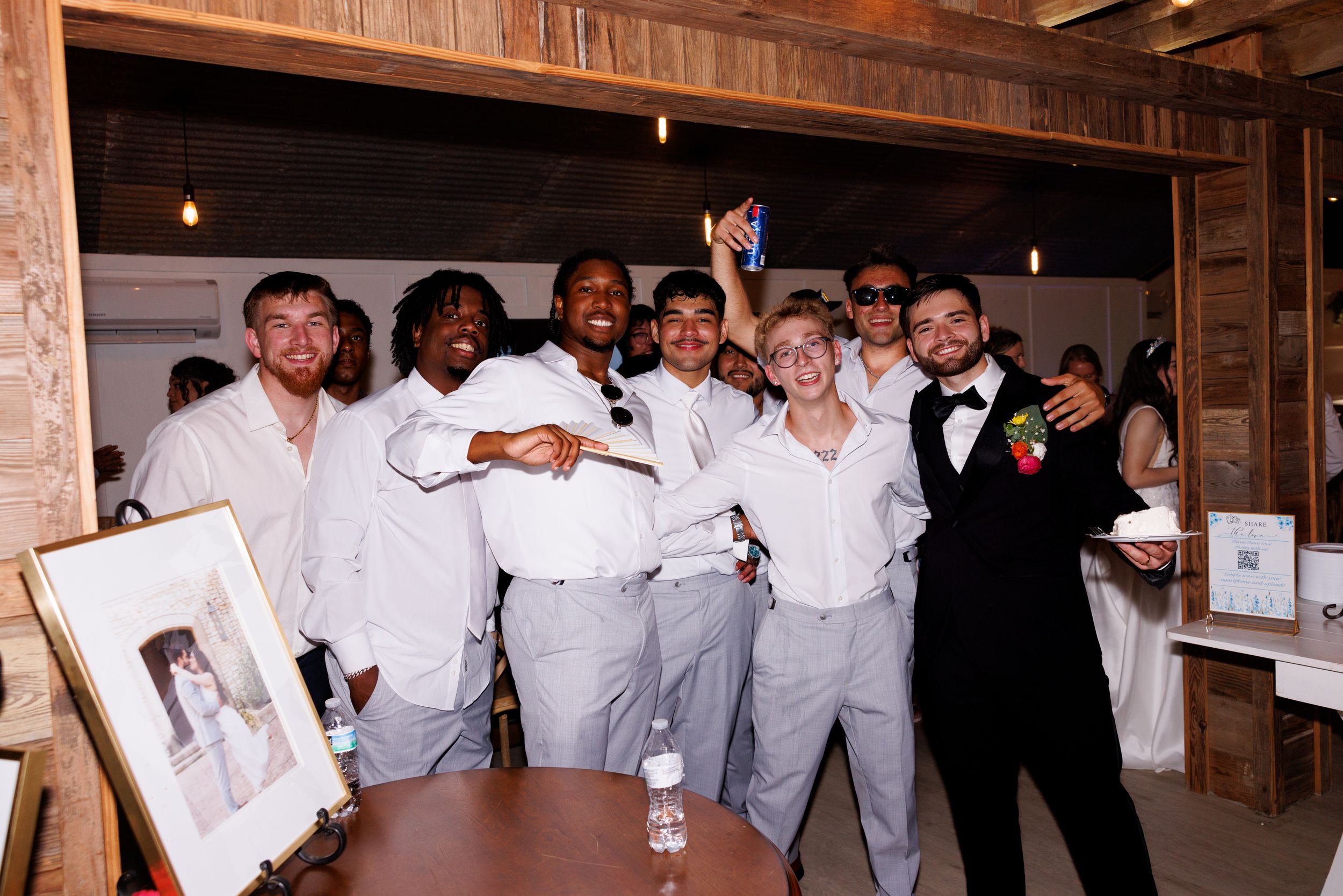 Wedding party celebrates in rustic barn venue with exposed wooden beams.