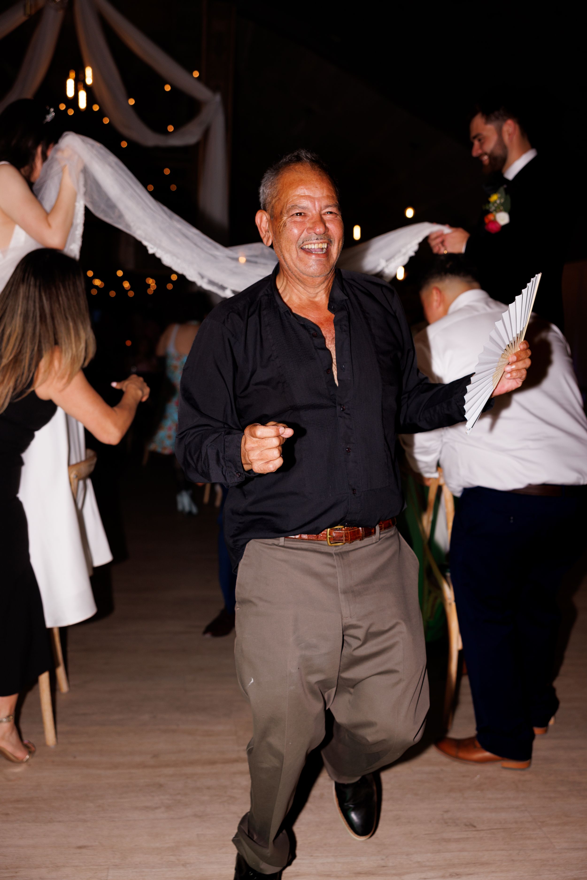 A guest in dark clothing dances joyfully at a wedding reception.
