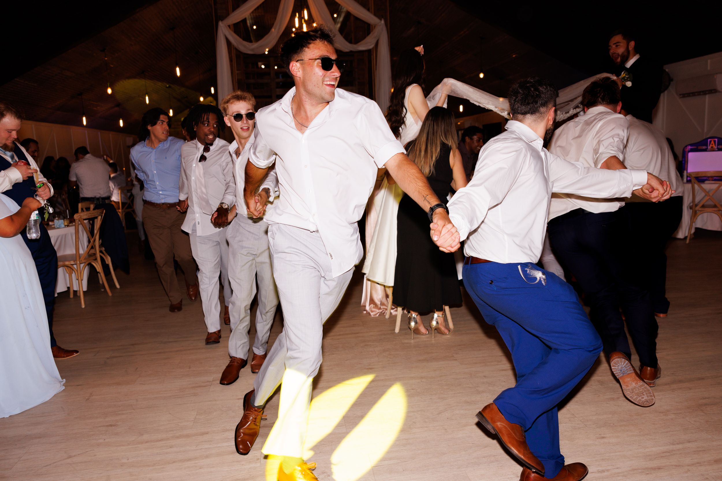 Wedding guests dance energetically on a wooden floor during the reception celebration.
