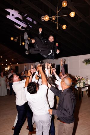 Party guests raise their hands in celebration while dancing under hanging lights.
