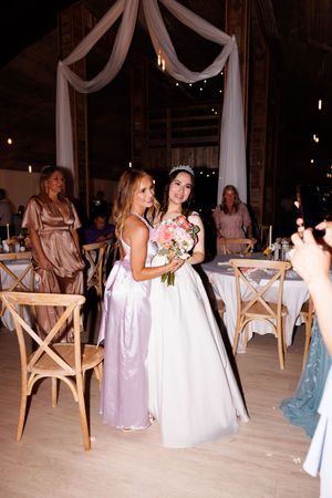 Wedding reception venue decorated with white drapes and wooden crossback chairs.