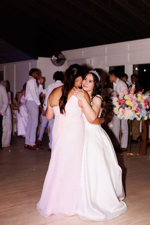Wedding guests dance together on a light-colored dance floor at an indoor reception venue.
