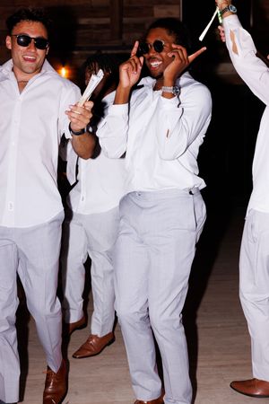 Groomsmen in all-white suits dance and celebrate at a wedding reception.