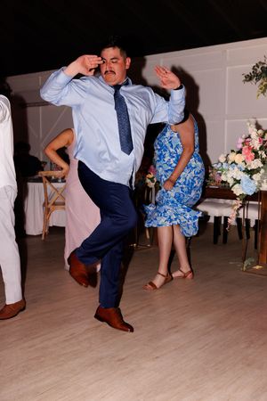 A man in a blue tie performs an energetic dance move on the wooden dance floor.