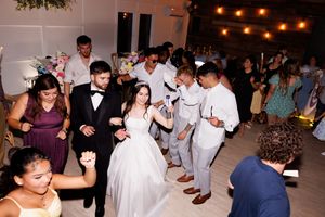 Wedding guests dance and celebrate on a light wooden dance floor under string lights.
