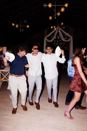 Party guests in formal attire dance in a line formation on a wooden floor.
