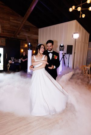 A couple shares their first dance at a wedding reception with dramatic fog effects on the dance floor.
