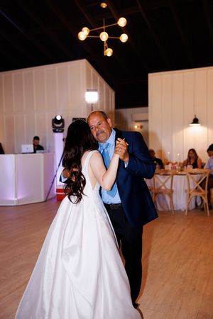 Wedding couple dances together in an elegant venue with wooden floors and white walls.