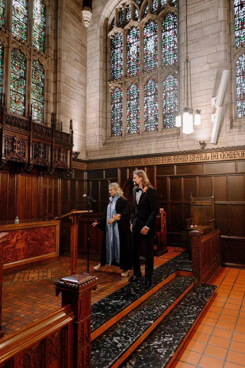 People stand inside the historic Gothic chapel interior with stained glass windows and dark wooden pews.