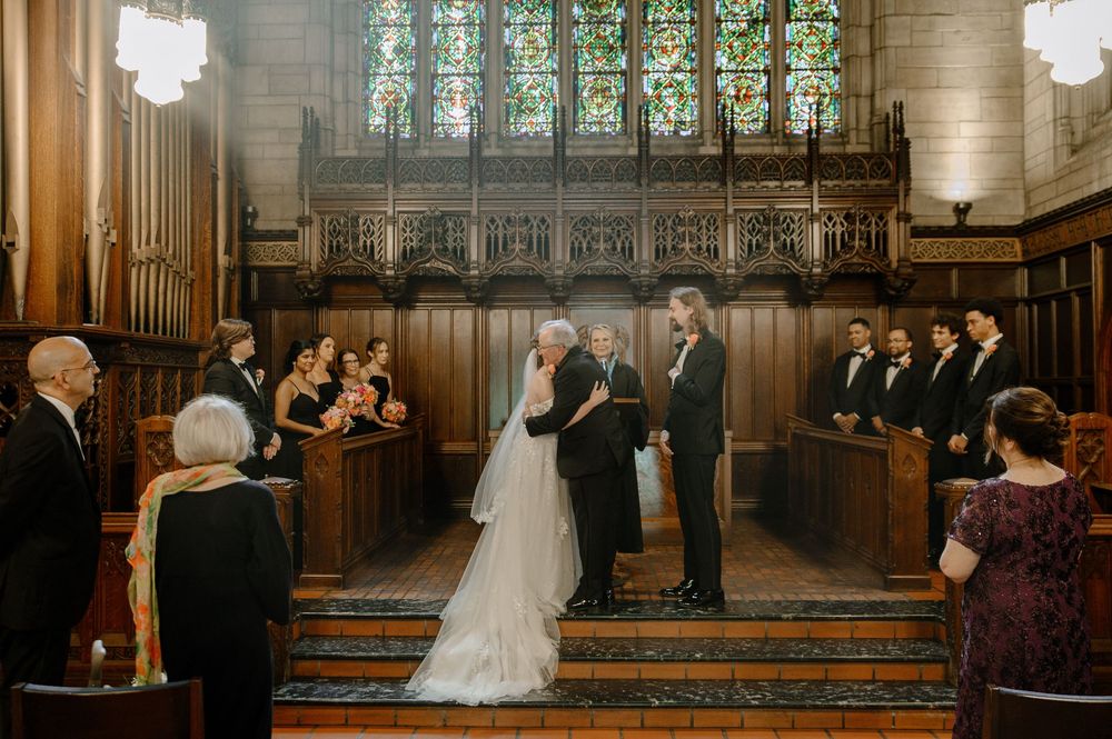 Traditional wedding ceremony taking place inside a grand cathedral with wooden paneling and stained glass windows.