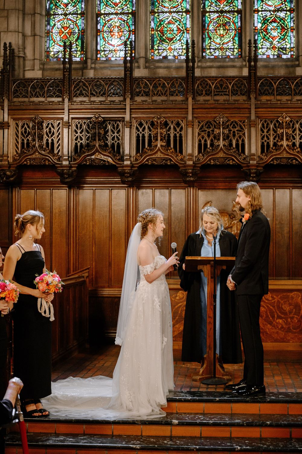 A wedding ceremony takes place in a cathedral with ornate wooden paneling and stained glass windows.