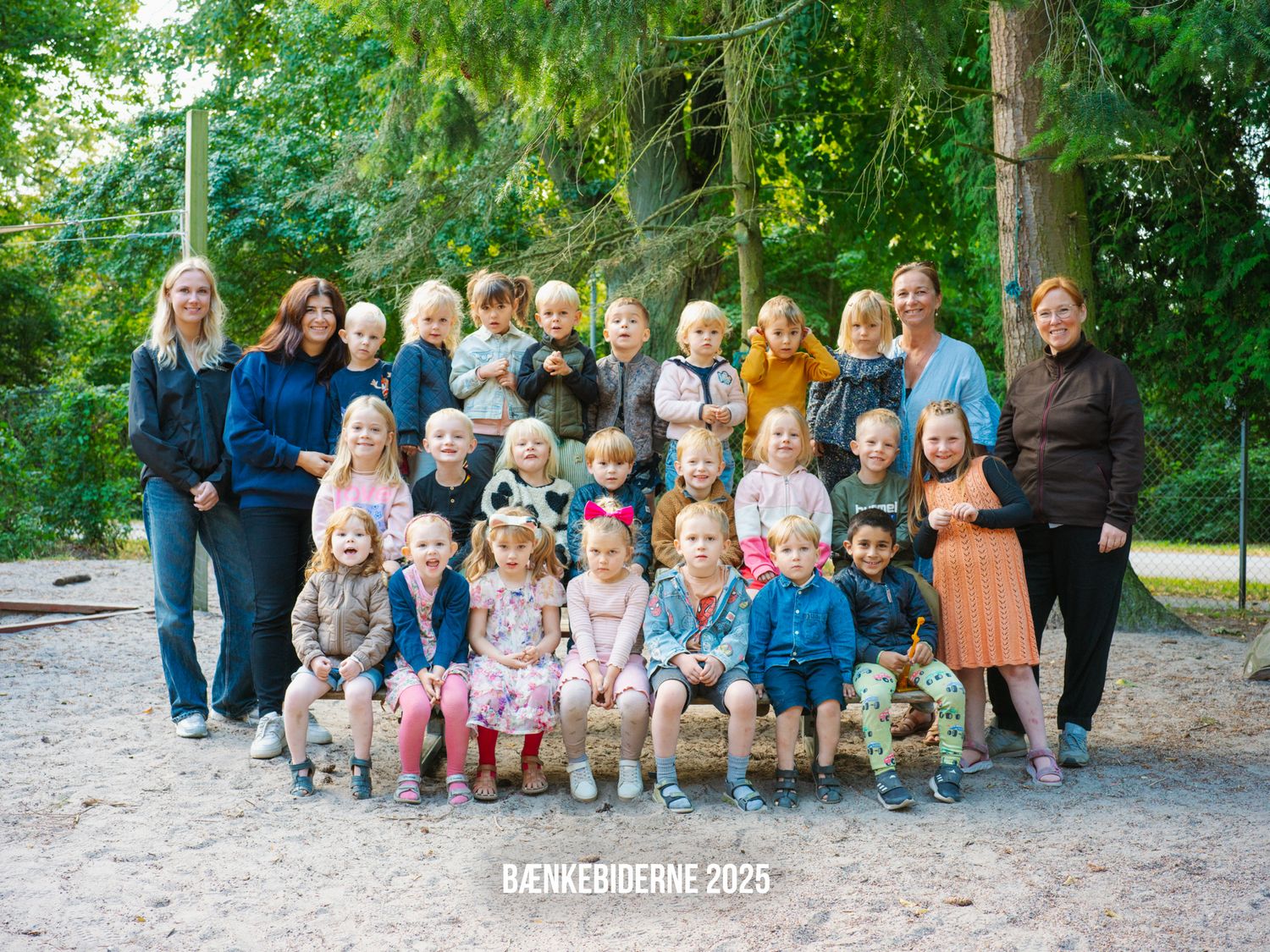 A group poses outdoors on a woodland path surrounded by green trees on a sunny day.