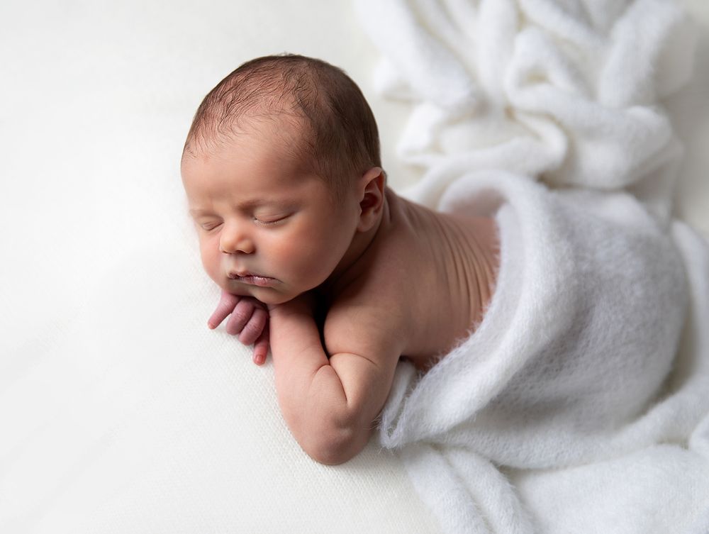 A peaceful sleeping newborn baby rests on soft white fabric in a professional portrait setting. At a newborn photography in Siscup