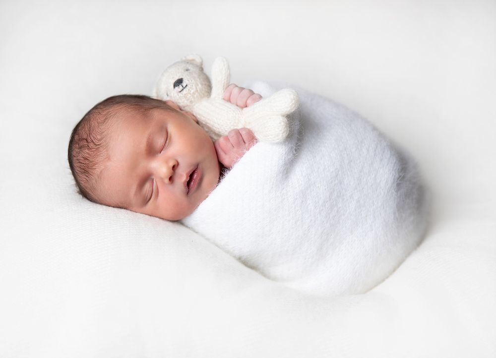 Sleeping newborn baby wrapped in white blanket on minimalist white background. During a newborn photoshoot in Sidcup