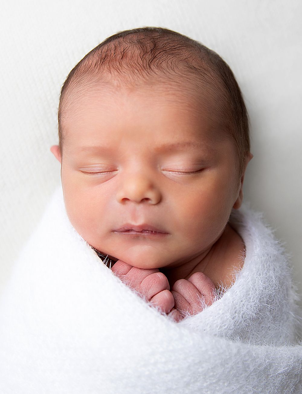 Peaceful sleeping newborn baby wrapped in soft white blanket against light background. During a newborn photoshoot in London