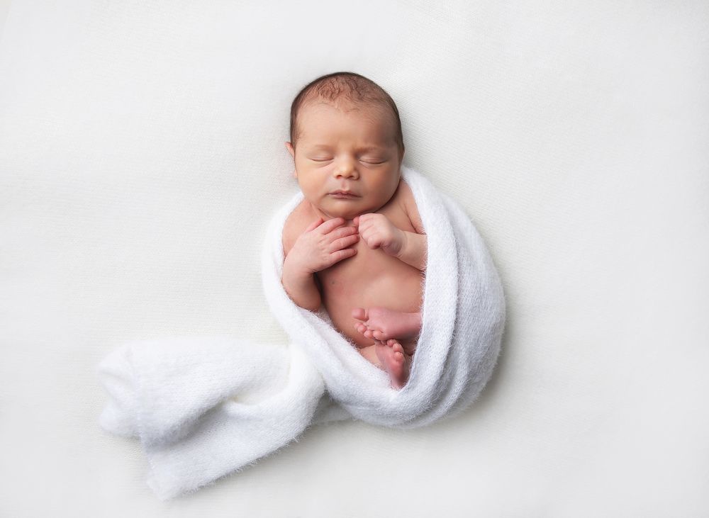 Series of peaceful newborn baby portraits in soft white swaddle against high key background. During a newborn photoshoot in Sidcup