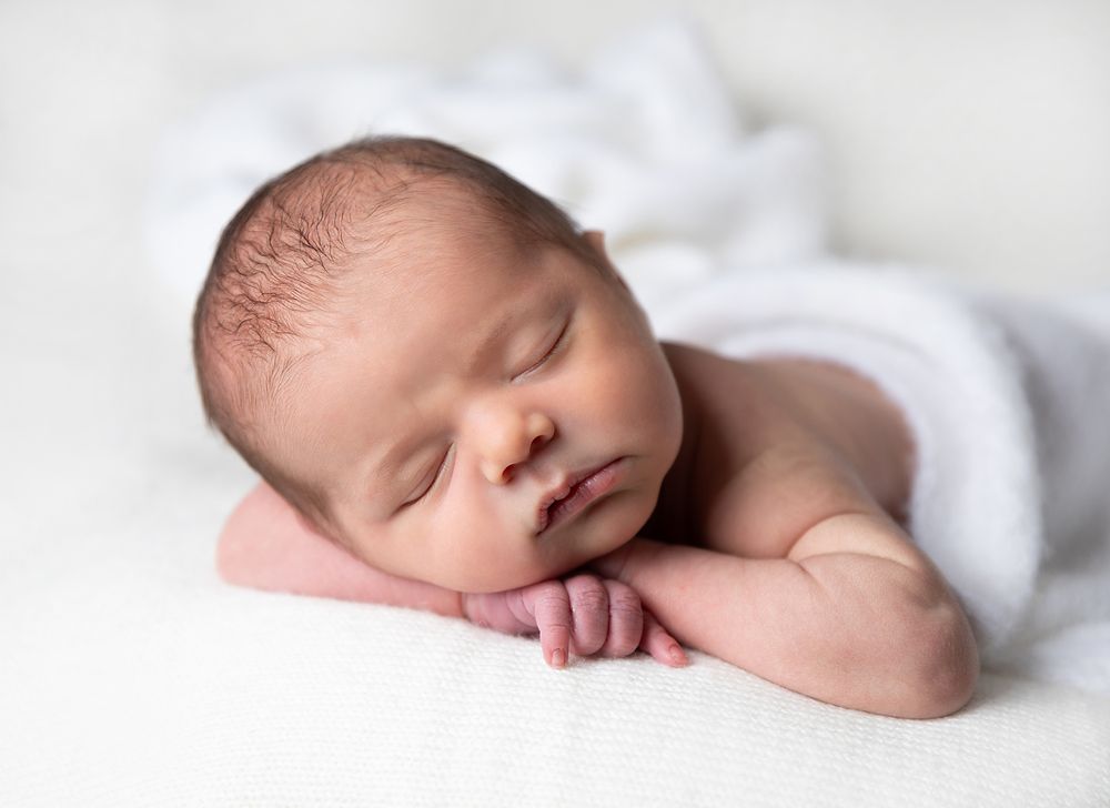 Professional newborn photography sequence showing peaceful sleeping baby wrapped in soft white blankets. During a newborn session in Sidcup