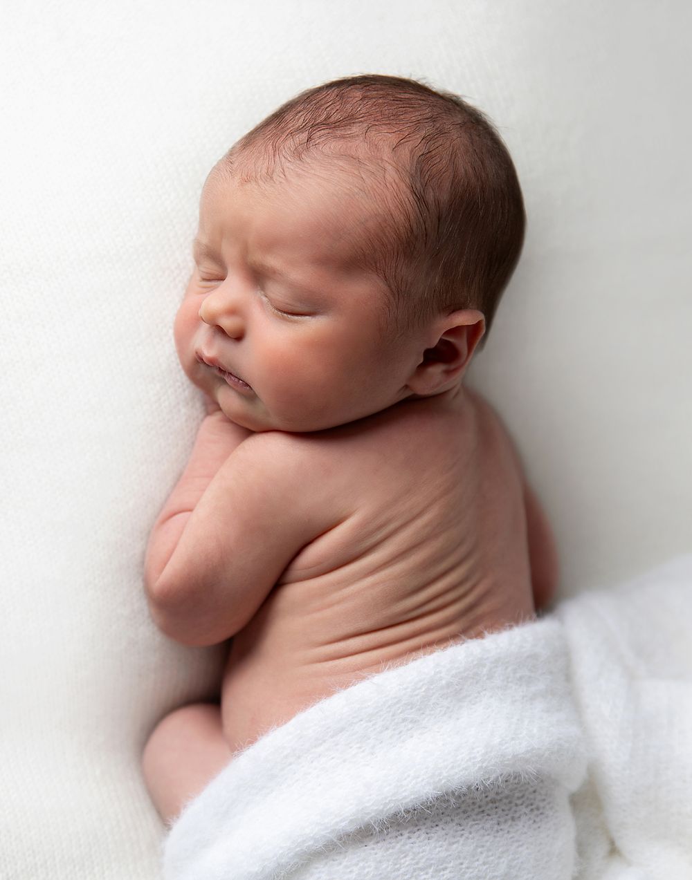 Newborn baby sleeping peacefully on white blanket in minimalist monochromatic portrait series. During a newborn photoshoot in Sidcup