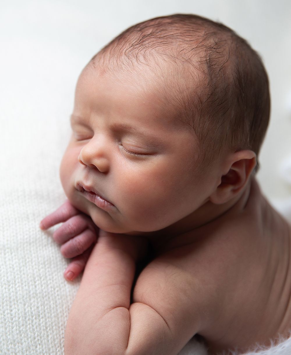 Peaceful sleeping newborn baby rests with closed eyes against soft white fabric. During a newborn photoshoot in Sidcup
