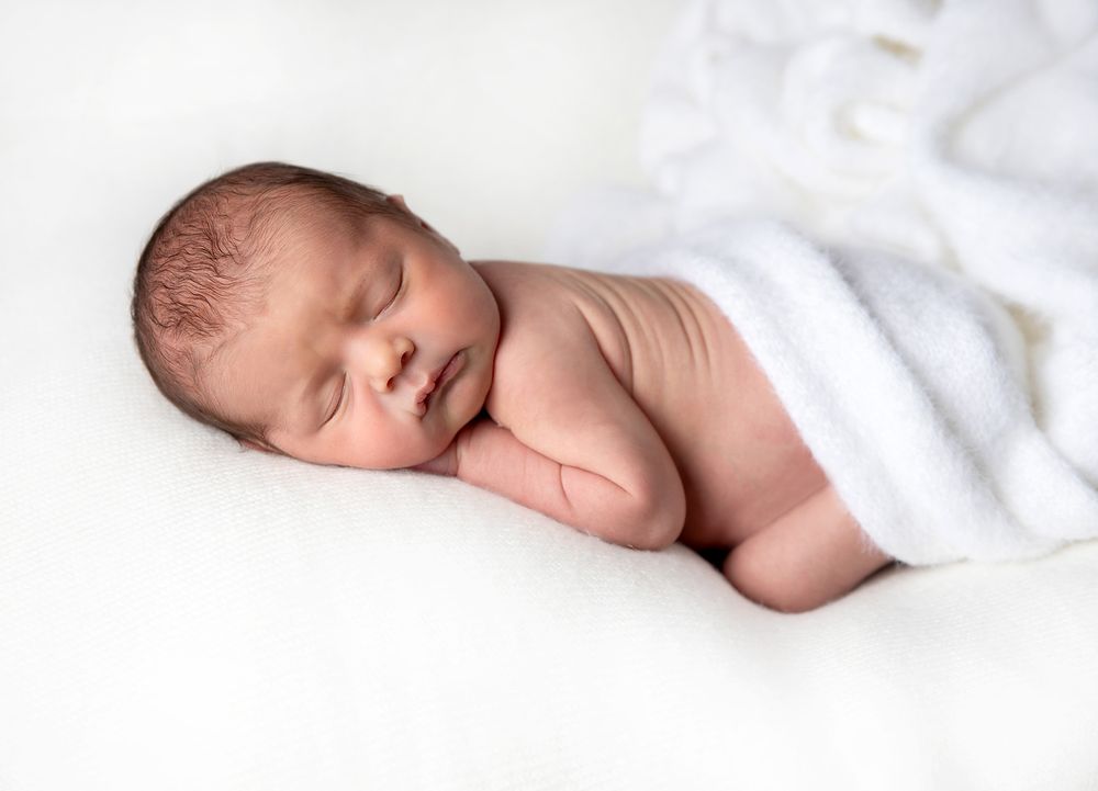 Peaceful newborn baby sleeping on white blanket during professional photo session. During a newborn photoshoot in Sidcup