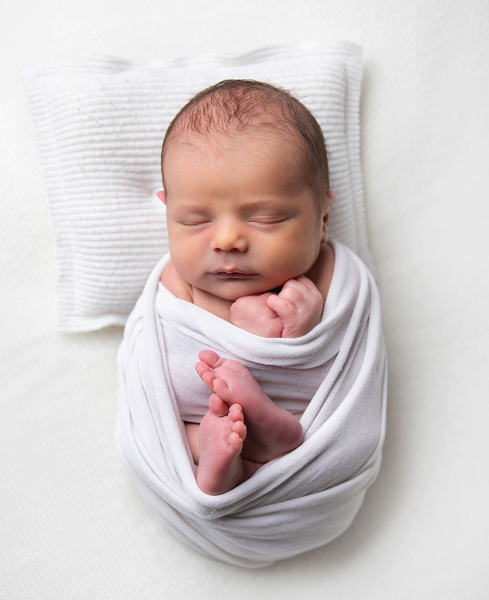 A sleeping newborn baby wrapped in soft white fabric shown from different angles in a series of peaceful photos. During a newborn photoshoot