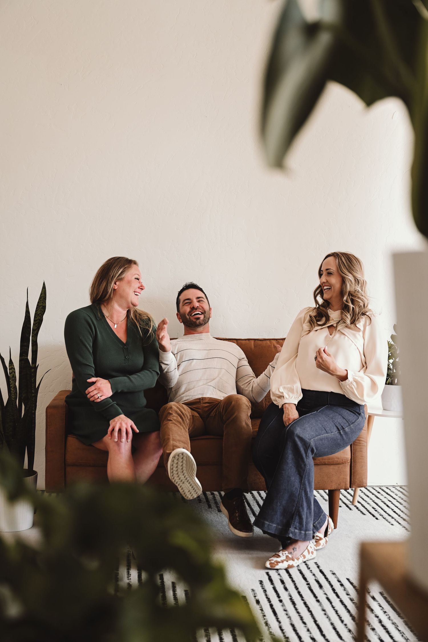 Playful couple lounges and laughs together on a brown leather couch in a bright modern room.