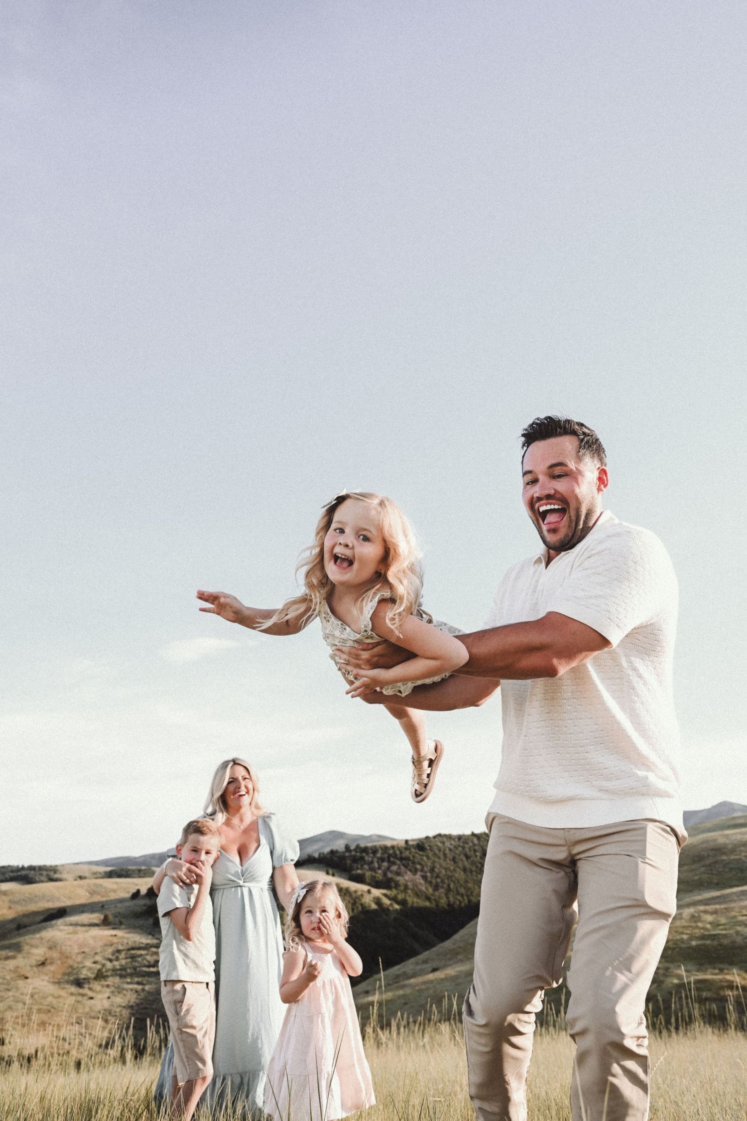 A joyful family playing and laughing together in a scenic mountain meadow landscape during golden hour.